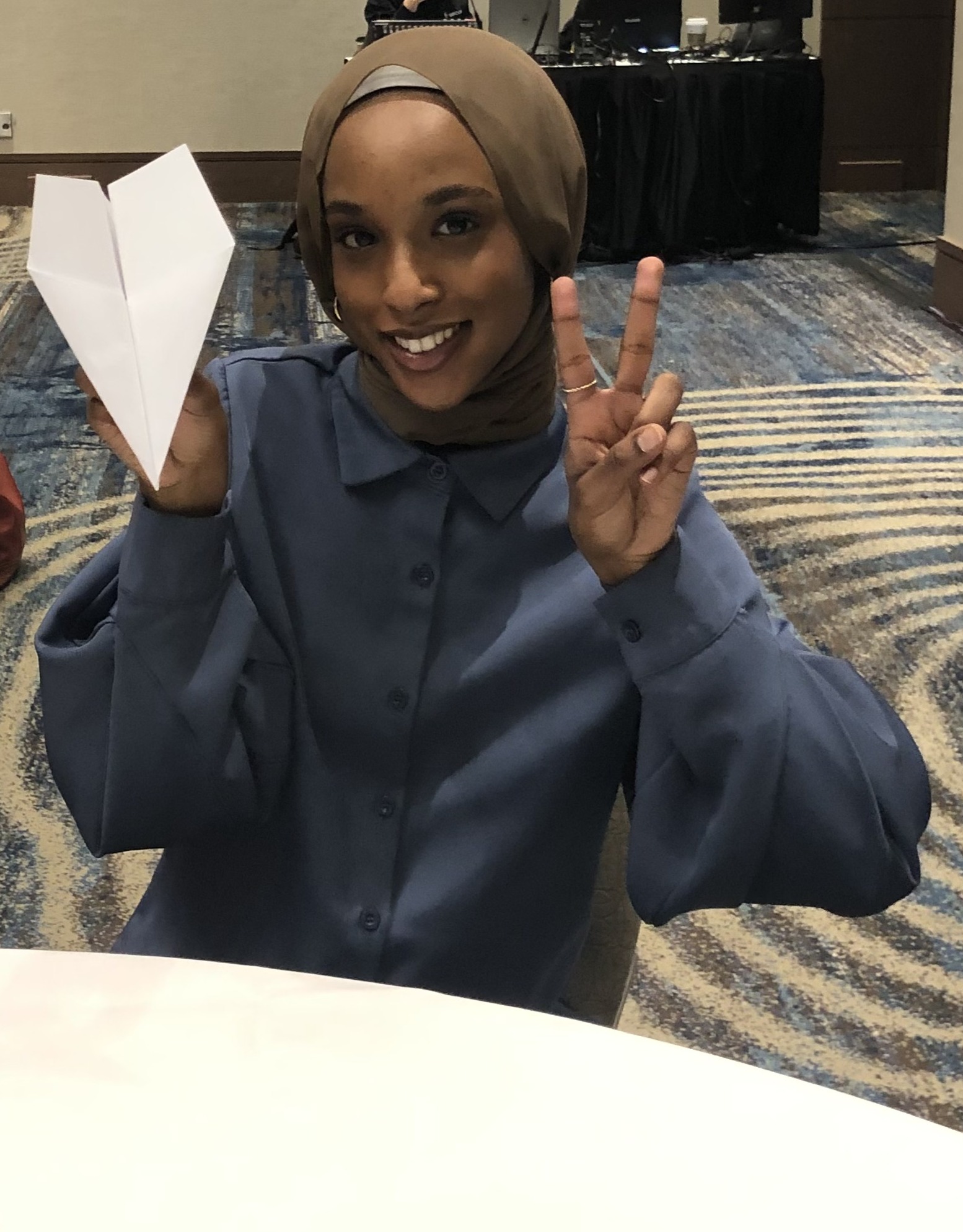 Une femme tenant un avion en papier fait un signe de la paix avec la main gauche.